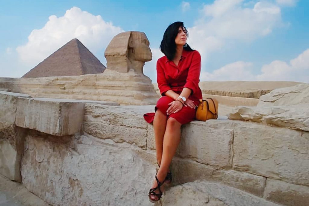 a girl is sitting next to the Pyramids and sphinx of Giza Egypt