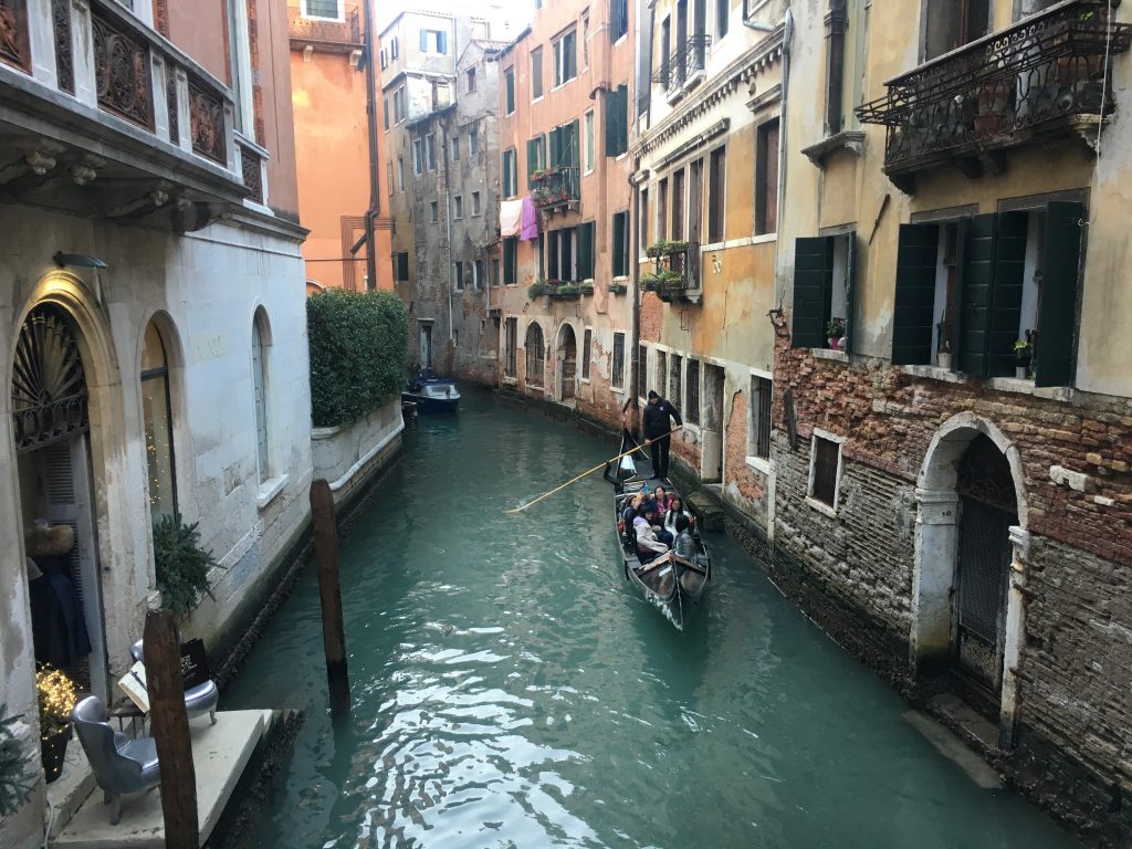 a man is riding a gondola in a small Venetian canal