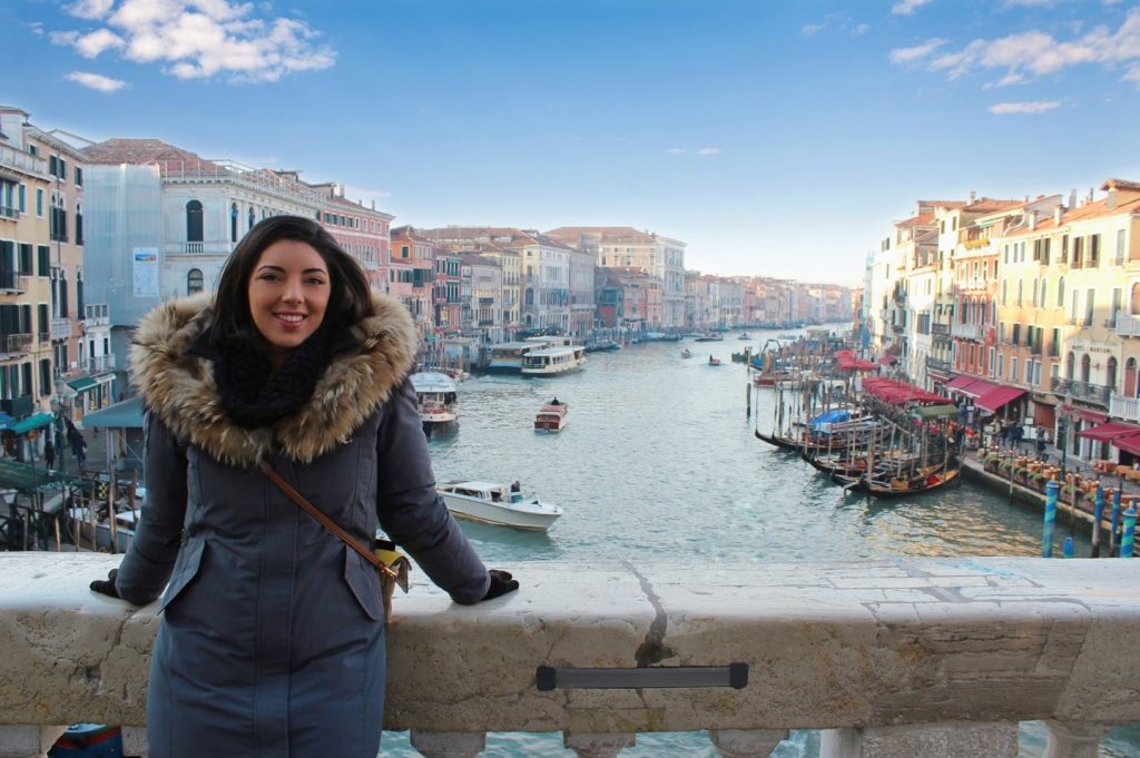 a girl is sitting on the Rialto bridge with view of the grand Canal in Venice