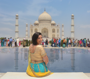 a girl is sitting on the bench in front of Taj Mahal