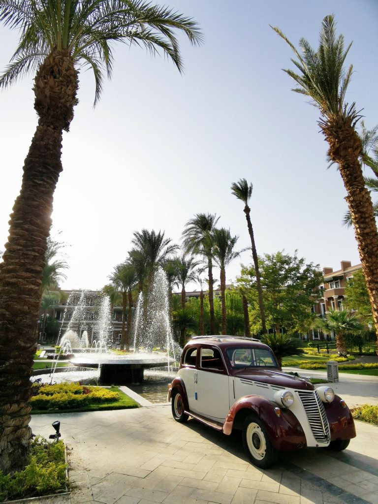 a classic car in front of the fountain and palm trees in the garden gate of the Sofitel Legend Old Cataract